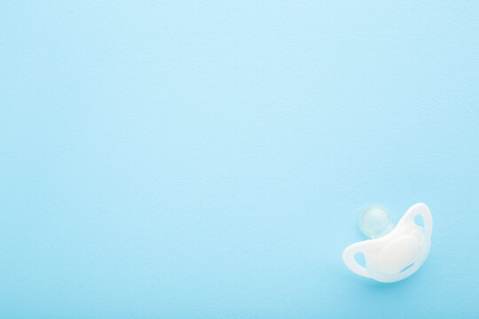 White silicone baby soother on light blue table background. Pastel color. First infant toy. Empty place for text. Top down view.