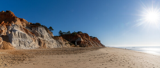 panorama view of a wide empty golden sand beach with colorful sand cliffs on a sunny day