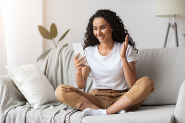 Positive young woman sitting on couch, having online call