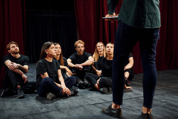 Fototapeta na wymiar Sitting and listening to man. Group of actors in dark colored clothes on rehearsal in the theater