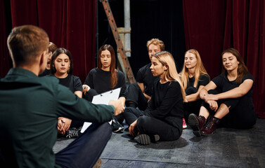 Sitting on the floor. Group of actors in dark colored clothes on rehearsal in the theater