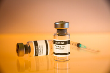 Covid-19 vaccine bottle and syringe on a yellow background