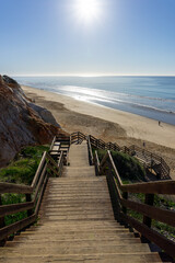 long wooden boardwalk beach access leading down to a wide golden beach with colorful sand cliffs