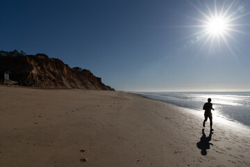 silhouette of a man jogging on an empty beach under the shining sun