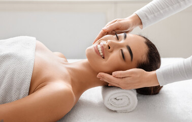 Smiling korean woman in spa salon enjoying relaxing head massage