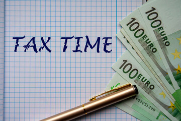 Hand written TAX TIME on checkered sheet paper with euro notes next to