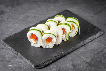 appetizing green sushi roll with philadelphia cheese cucumber and salmon on a black stone plate