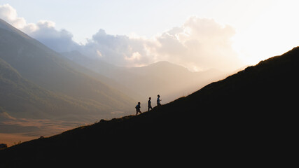 Silhouette of three men climbing a mountain at sunset 