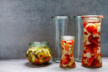 Glass jars of various shapes with vegetable pickles. Homemade food preserved. Few empty jars.