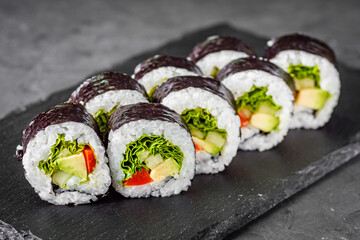 appetizing vegan sushi roll futomaki with pepper cucumber and avocado salad on a black stone plate