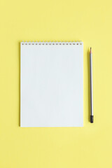 Notebook with blank page and pencil on a yellow background.