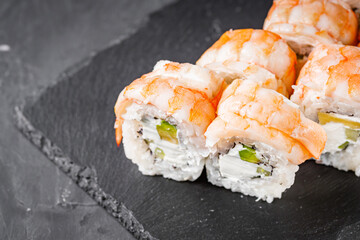 appetizing sushi roll philadelphia with avocado cheese cucumber and shrimp on a black stone plate