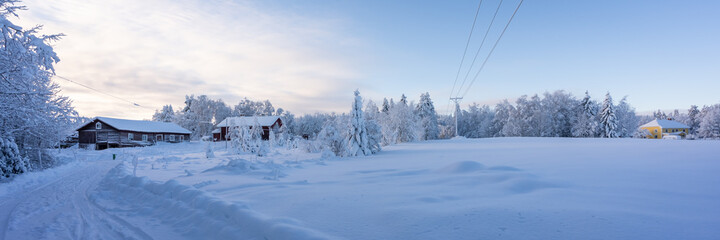 Winter snowy morning in the country side in Sweden. Traditional typical Scandinavian house in winter. Old wooden red house cottage on blue sky background. Sun is rising.