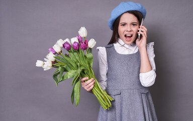 Funny young Caucasian lady in a stylish blue hat in a beret with a phone holds tulips flowers in...