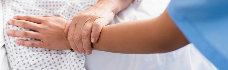 cropped view of aged woman touching hand of nurse in hospital, banner