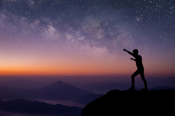 Fototapeta premium Silhouette of young traveler standing and open arms and watched the star and milky way on top of the mountain before sunrise. He is happy to be with herself and stay with nature at twilight time.