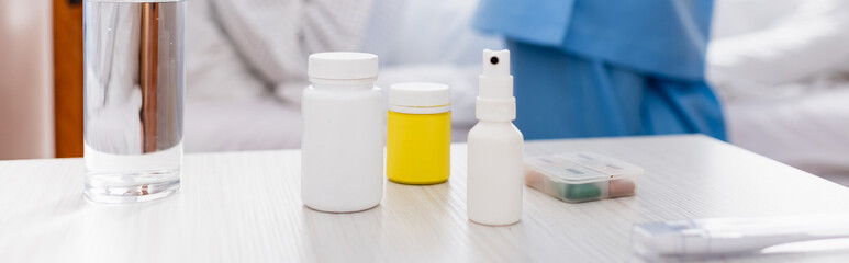 glass of water, containers with medicines, throat spray and thermometer on table in hospital, banner