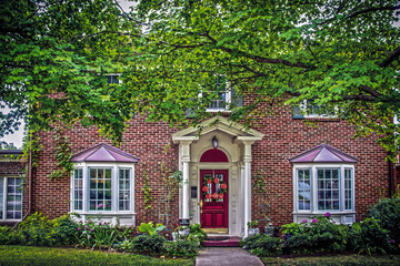Traditional brick house with bay windows and pillars in summer with landscaping and door wreath and No soliciting sign and large maple trees