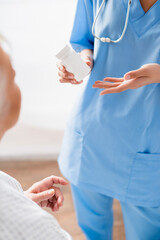 partial view of nurse pointing at container with medicines near elderly woman on blurred foreground