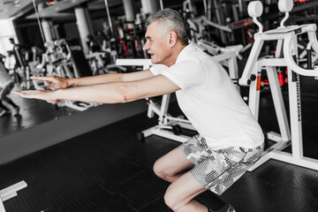 Photo of a man with gray hair performing an exercise squatting in the gym