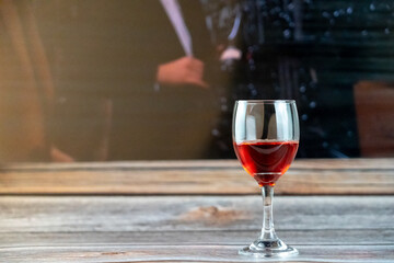 glass with red wine on the table and the customer is collecting wine on the background.