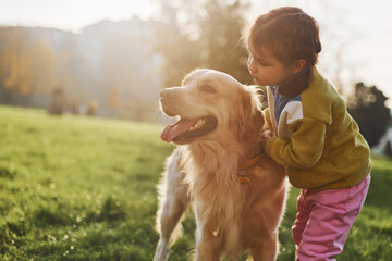 Little girl have a walk with Golden Retriever dog in the park at daytime