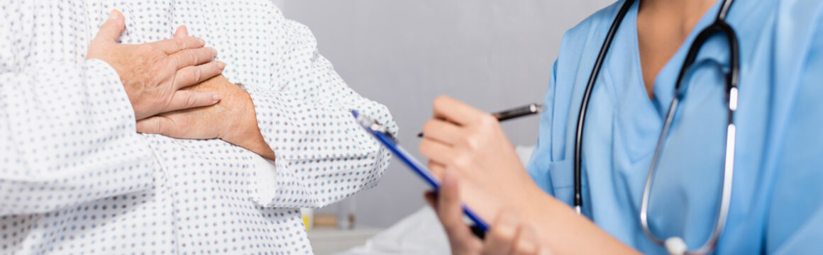 cropped view of senior woman touching chest while suffering from gasp attack near nurse writing on clipboard, blurred foreground, banner