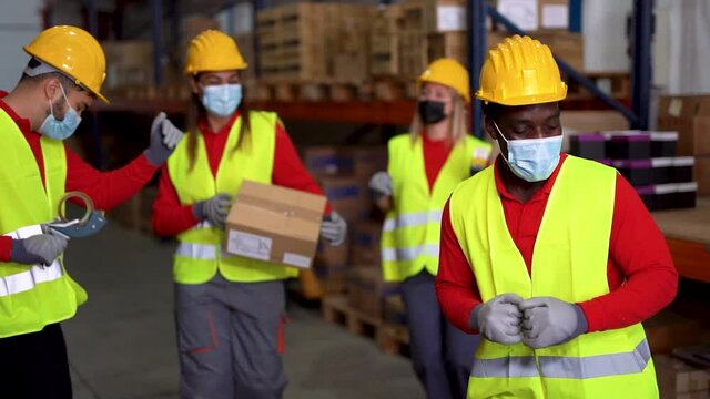 Happy multiracial staff dancing in warehouse while wearing protective face masks for coronavirus - Fun and happiness