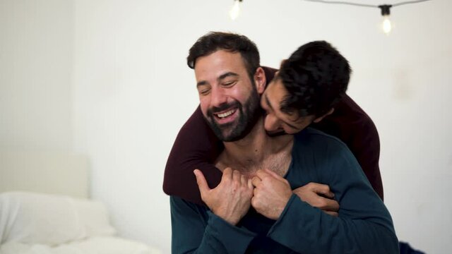 Gay men couple hugging each other at home in bedroom while wearing pyjama - Homosexual love  and lifestyle concept
