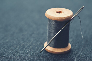 Wooden spool of blue thread on blue jeans cloth. Needle and thread through.
