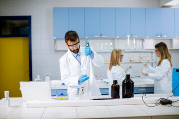 Young researcher in protective workwear standing in the laboratory and analyzing flask with liquid