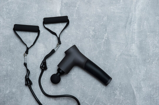 Therapeutic massage gun and rubber resistance bands on grey background with copy space. Fitness sport concept.