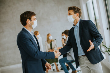 Young business men handshaking in the office with protective facial masks