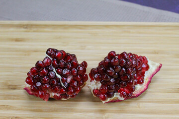 Two pieces of pomegranate with red seeds on a wooden tray. Pomegranate seeds. One piece next to...