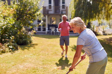 Retired Man Bringing Cold Drink To Woman Tidying Garden With Rake