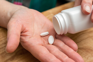 White pills of painkiller or antibiotic for treatment on senior woman hand palm, medicines and vitamin supplements concept, close-up view