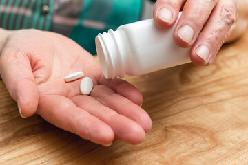 White pills of painkiller or antibiotic for treatment on senior woman hand palm, medicines and vitamin supplements concept, close-up view