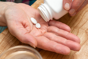 White pills of painkiller or antibiotic for treatment on senior woman hand palm, medicines and vitamin supplements concept, close-up view
