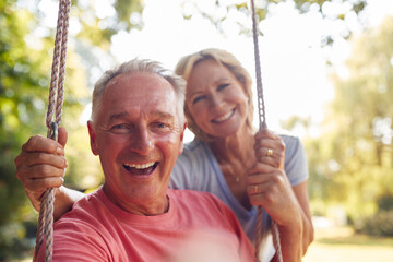 Portrait Of Retired Couple Having Fun With Woman Pushing Man On Garden Swing - obrazy, fototapety, plakaty