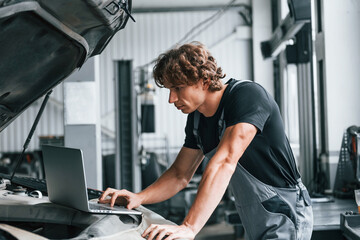 Using computer. Adult man in grey colored uniform works in the automobile salon
