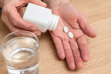 White pills of painkiller or antibiotic for treatment on senior woman hand palm, glass with water, medicines and vitamin supplements concept,close-up view