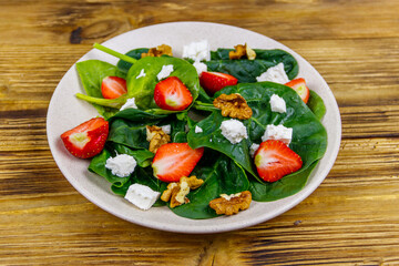 Fresh healthy salad with strawberry, spinach, walnuts and feta cheese on wooden table