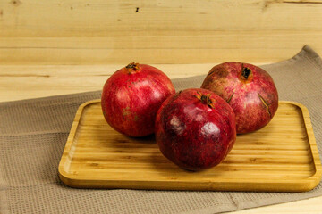Three ripe pomegranate fruits. Red large pomegranates. Pomegranates on a wooden tray, with all the tablecloth underneath. Whole pomegranate fruit.