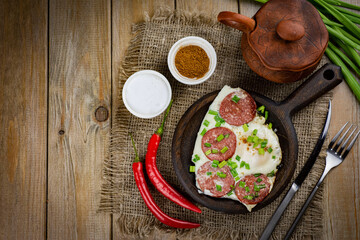 Rich breakfast: fried eggs with sausage and herbs on a wooden table