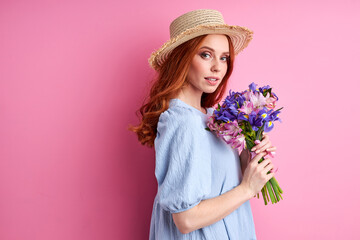 female with summer flowers posing on pink background, attractive lady in hat having charming look