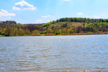 Spring landscape with beautiful lake, green meadows, hills, trees and blue sky