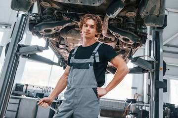 Handsome adult man in grey colored uniform standing below automobile