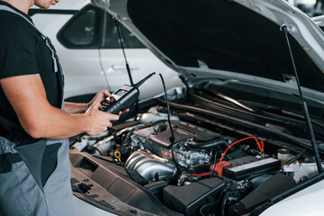 Special tool for testing characteristics. Adult man in grey colored uniform works in the automobile...
