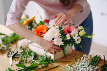 Florist at work: young brunette woman hands making fashion modern composition of different flowers at home