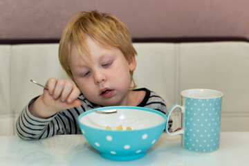 The child looks at the fork which he eats from the plate